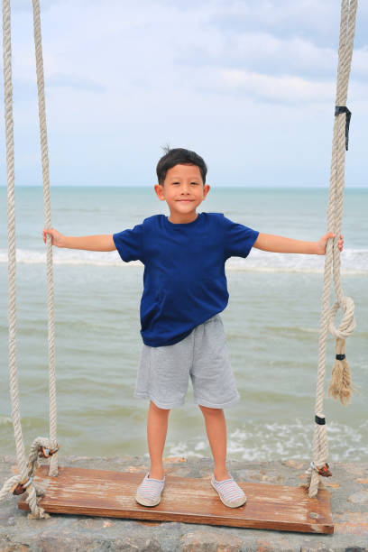 istock Asian little boy play standing on swing against cement wall at seaside. 1831778004
