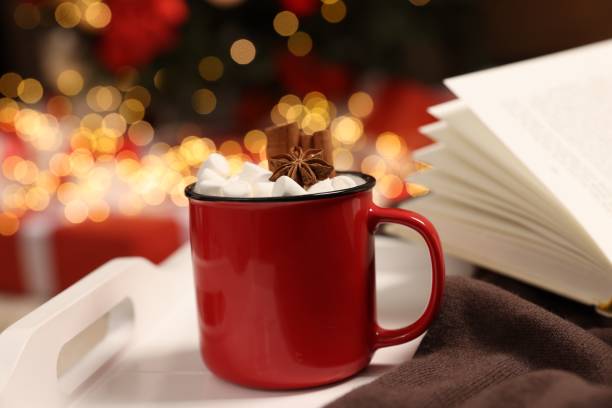 istock Delicious cocoa with marshmallows, cinnamon sticks and anise star in cup on white tray against blurred Christmas lights, closeup 1831781237