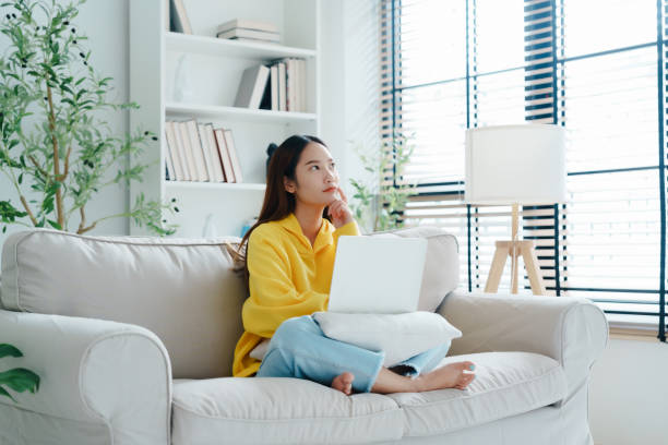 istock Happy young Asian woman using laptop while seated on couch at home 1831803916