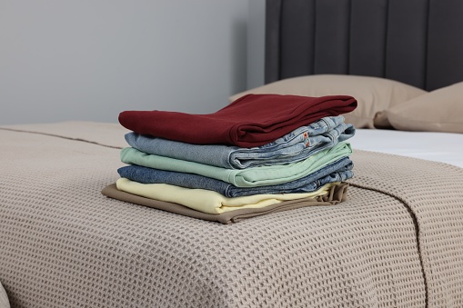 Stack of different folded clothes on bed indoors
