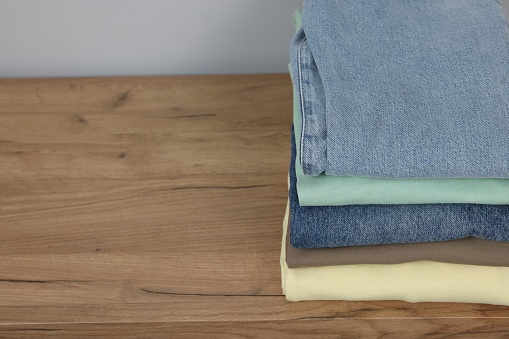 Stack of different folded clothes on wooden table near grey wall, closeup. Space for text