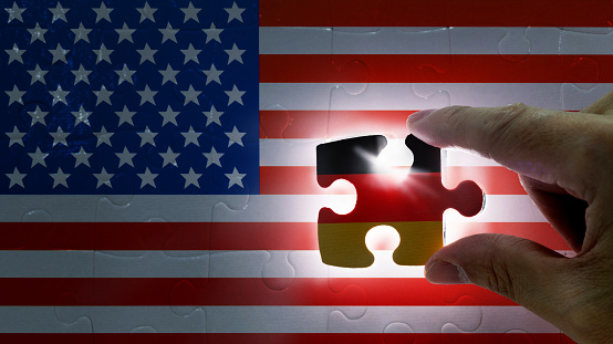 Hand holding piece of jigsaw puzzle with flag of Germany closing to the USA