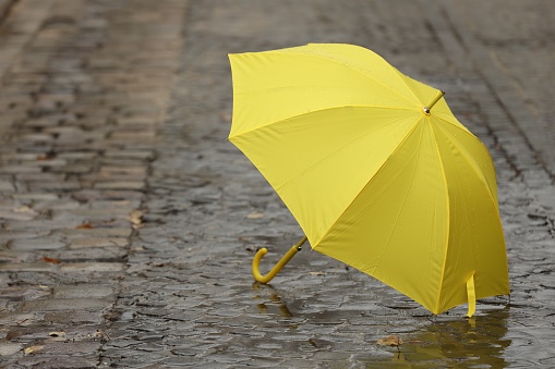 Open yellow umbrella on wet pavement. Space for text