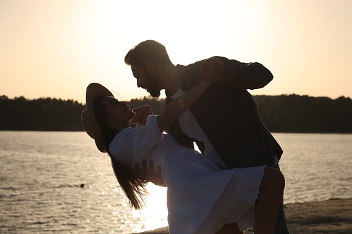 Happy couple dancing near river at sunset