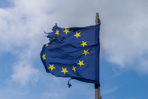 A torn EU flag blows in the wind with a few clouds in the background, seen in Pevensey Bay, East Sussex, England, UK
