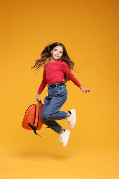 istock Back to school. Cute girl with backpack jumping on orange background 1831891840