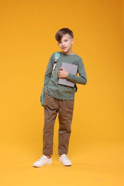 istock Cute schoolboy with book on orange background 1831894404