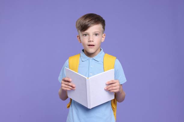 istock Cute schoolboy with book on violet background 1831896466