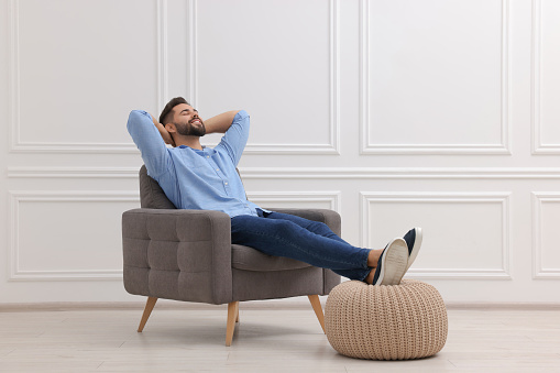 Handsome man relaxing in armchair near white wall indoors