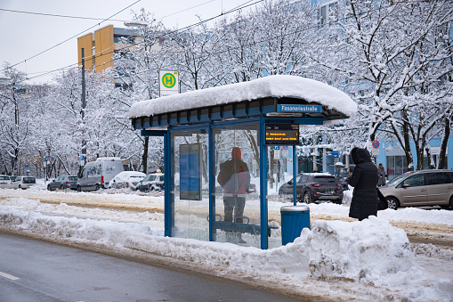 Winter scene in the snowy streets of Munich, Bavaria, Germany.  A tram and bus stop, waiting passengers, snow-covered bus shelter