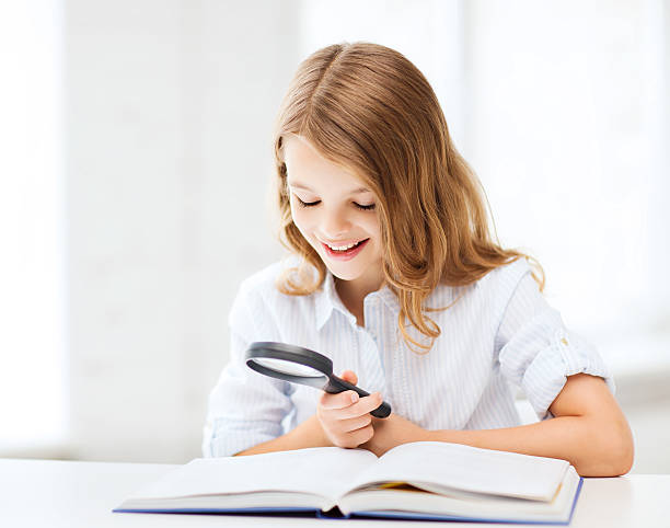 istock girl reading book with magnifier at school 183194157