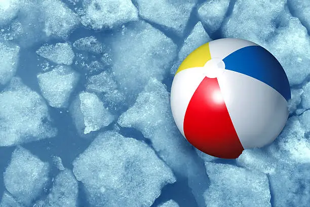 Cold summer weather concept with a plastic inflatabe beach ball stuck in frozen ice in a freezing pool as a symbol of leisure activity problems caused by colder temperatures during vacations and family holidays.