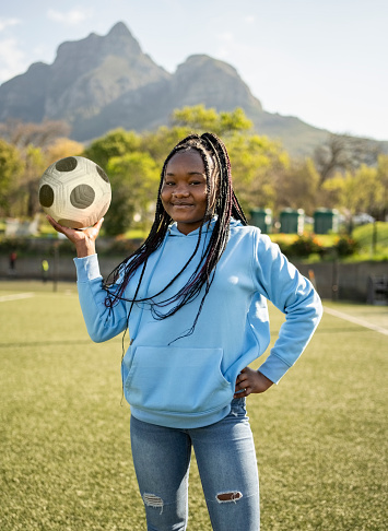 Portrait of beautiful young african girl holding ball standing on field an looking at camera outside