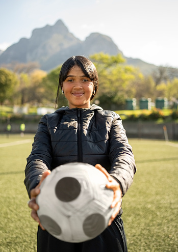 Portrait of smiling young girl holding a soccer ball in front on outdoor field