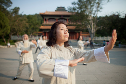 A senior couple take their Tai Chi outdoors on a warm summers day as they enjoy the fresh air.  They are both dressed casually and are focused on their movements and breathing.