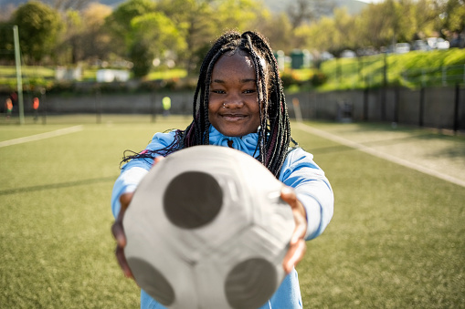 Portrait of african girl soccer player holding a soccer ball in front on outdoor field and looking at camera
