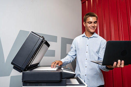 Positive young man using printer in the modern office close up