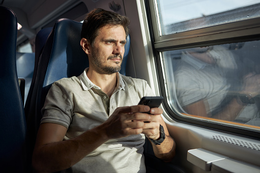 Young male tourist using smart phone while traveling by subway train.