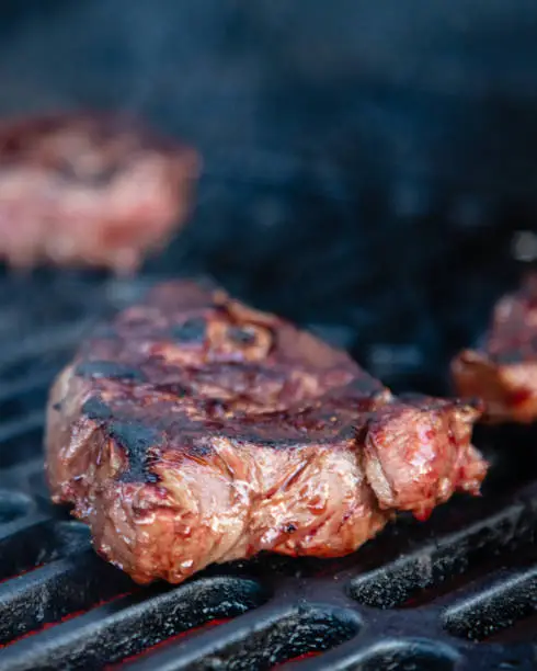 Rumpsteak is cooked on a charcoal grill on a cast iron grate. Close-up.