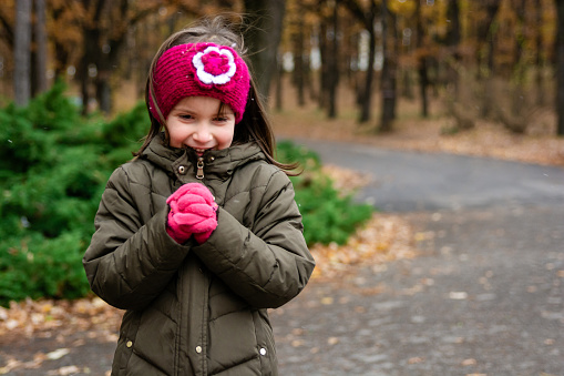 A cute little girl is freezing while standing outside in the park on a cold winter day