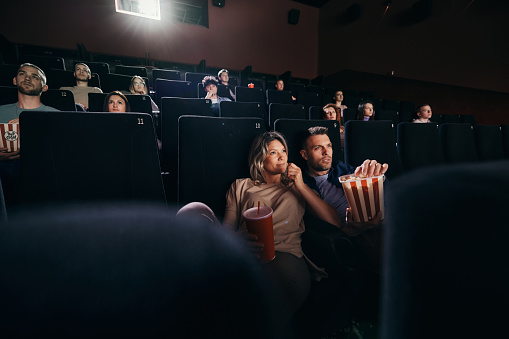 Large group of people watching a movie projection in theatre. Focus is on relaxed couple.