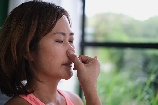 Close-up shot of Mature Asian woman holding the nose while doing pranayama breathing exercise at home.