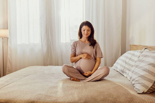 istock Smiling expecting woman holding her stomach on a bed. 1832112218