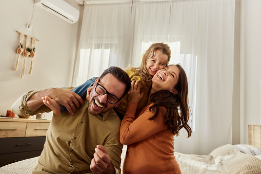 Cheerful girl having fun with her parents in bedroom. Copy space.