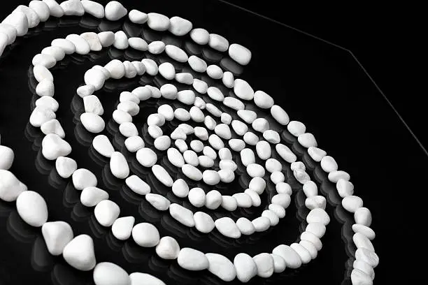 Spiral made from white marble peblles on black reflective table. Focus on the midle of spiral.