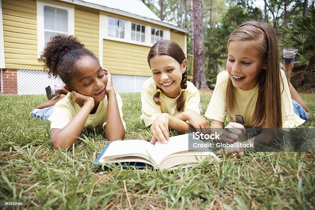 Allegro giovane ragazza leggendo il libro mentre Sdraiato su un prato - Foto stock royalty-free di Adolescente
