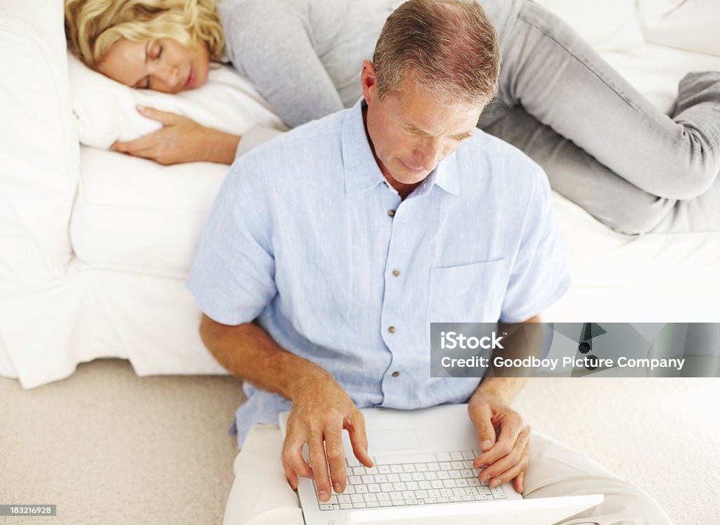 Dojrzały mężczyzna pracujący z laptopa, podczas gdy kobieta śpi na kanapie - Zbiór zdjęć royalty-free (40-49 lat)