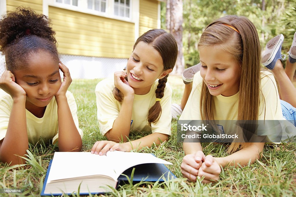 Três jovens mulheres deitado na grama, lendo livro - Foto de stock de Adolescente royalty-free