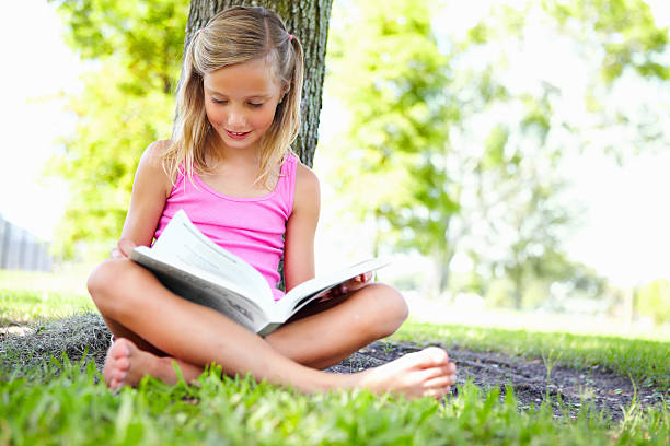 istock Happy young girl reading book under the tree 183218736