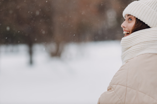 Happy smiling young woman profile portrait dressed coat scarf hat and mittens enjoys winter weather at snowy winter park