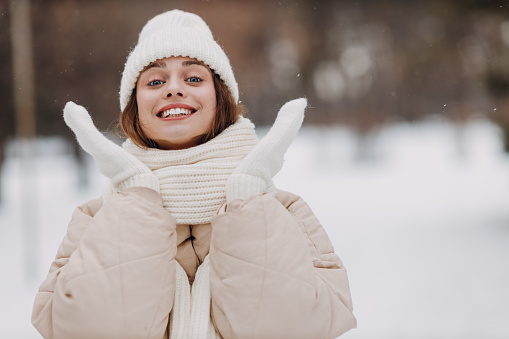 Happy smiling young woman portrait dressed coat scarf hat and mittens enjoys winter weather at snowy winter park