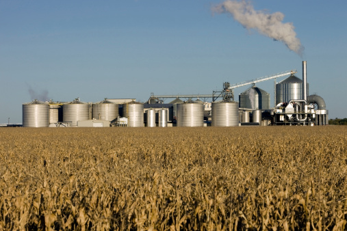Agricultural Silos on the background of the field. Storage and drying of grains, wheat, corn, soy, sunflower against the blue sky with white clouds. Storage of the crop.