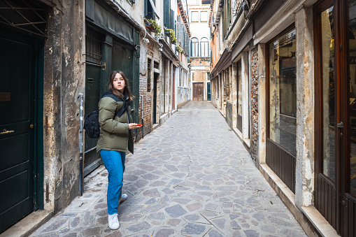 Beautiful teenage girl standing in the narrow stone paved street 