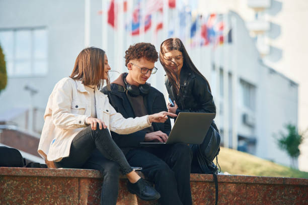 istock Sitting and using laptop. Three young students are outside the university outdoors 1832222713