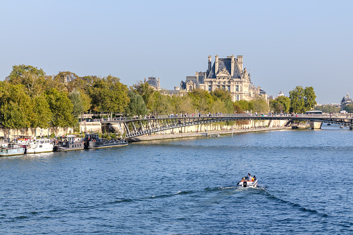 Paris, France - October 8, 2023 : View of a small boat at the Seine river, a pedestrian bridge and the City Hall of Paris France in the background