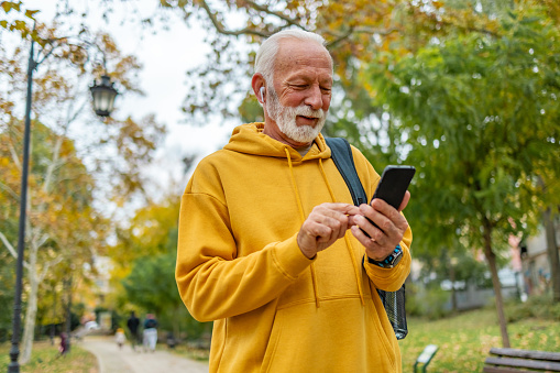Smiling senior man using phone while standing in public park