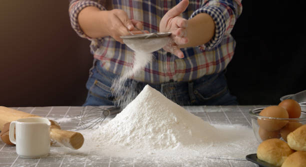 istock artisan bread working with dough. Use a sieve to sift flour into dough handmade bread with bakery equipment tools, black background. Bread-making process for baker at work. 1832275580