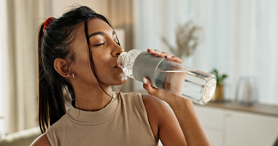 Drinking water, yoga or Indian woman in home with health, fitness or wellness for natural hydration. Thirsty female person, tired or healthy girl with liquid bottle after pilates to detox or relax