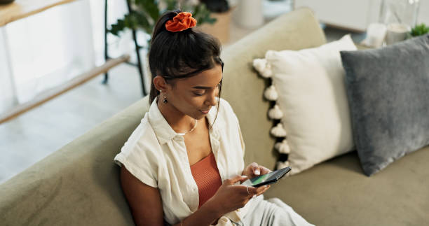 istock Woman, typing and scroll on smartphone in home for social network, update multimedia subscription or chat on sofa from above. Indian girl, phone and download mobile games, reading notification or app 1832280821