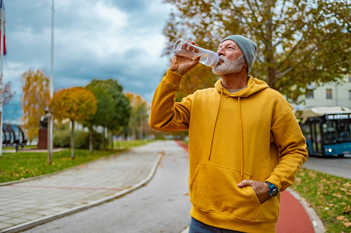 Senior fitness man drinking water outdoors.
