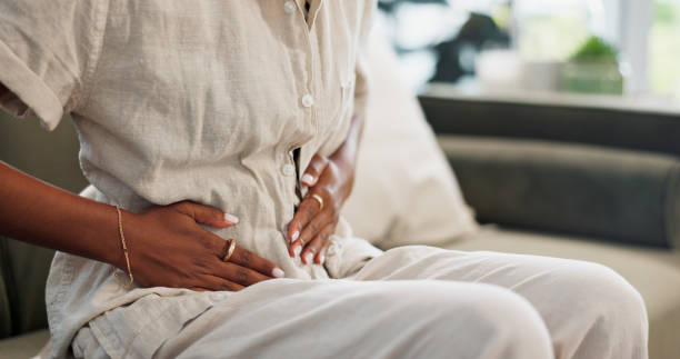 stomach pain, woman and hands on couch at home with abdomen problem and constipation from virus. sick person, menstruation and bloated belly ache from colon health issue and cramps in a living room - indigestie fotos stockfoto's en -beelden