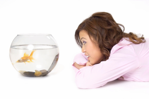 Young woman watching a goldfish in a fishbowl.