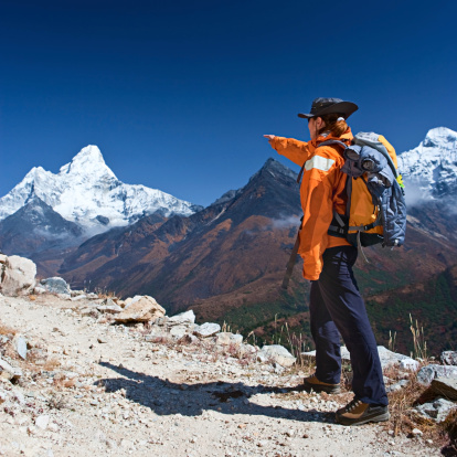 Female trekker pointing at mount Ama Dablam in Mount Everest National Park, Nepal. This is the highest national park in the world, with the  entire park located above 3,000 m ( 9,700 ft). This park includes three peaks higher than 8,000 m, including Mt  Everest. Therefore, most of the park area is very rugged and steep, with its terrain cut by deep rivers and  glaciers. Unlike other parks in the plain areas, this park can be divided into four climate zones because of the  rising altitude. The climatic zones include a forested lower zone, a zone of alpine scrub, the upper alpine zone  which includes upper limit of vegetation growth, and the Arctic zone where no plants can grow.http://bem.2be.pl/IS/nepal_380.jpg