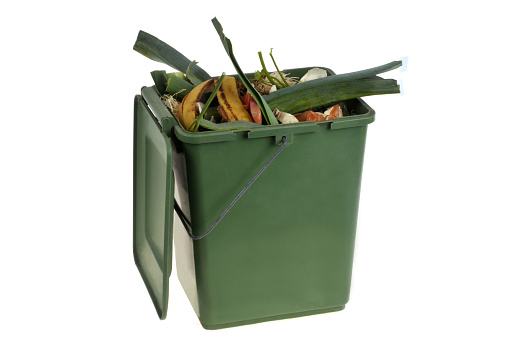 Composting concept with a green plastic container filled with organic waste close-up on a white background