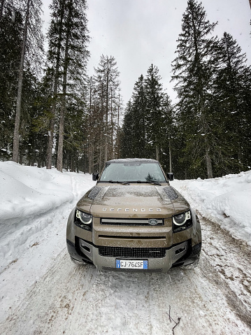 Sexten, Italy - February 2, 2023 : The New Land Rover Defender parked in a country road close to an alpine forest during a snowfall