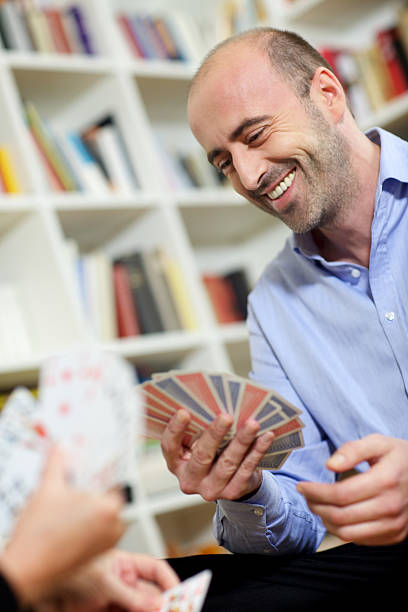 istock laughing mature Man with stubble and bald plays cards 183236015